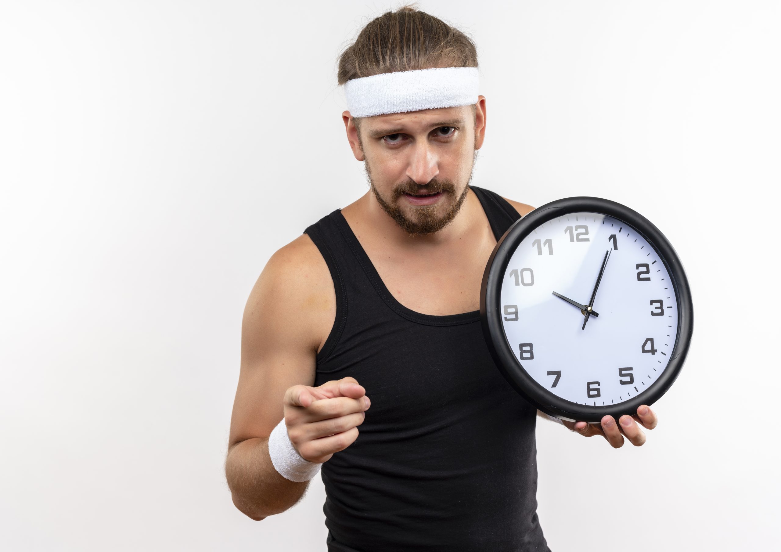 confident-young-handsome-sporty-man-wearing-headband-wristbands-holding-clock-pointing-isolated-white-wall-with-copy-space