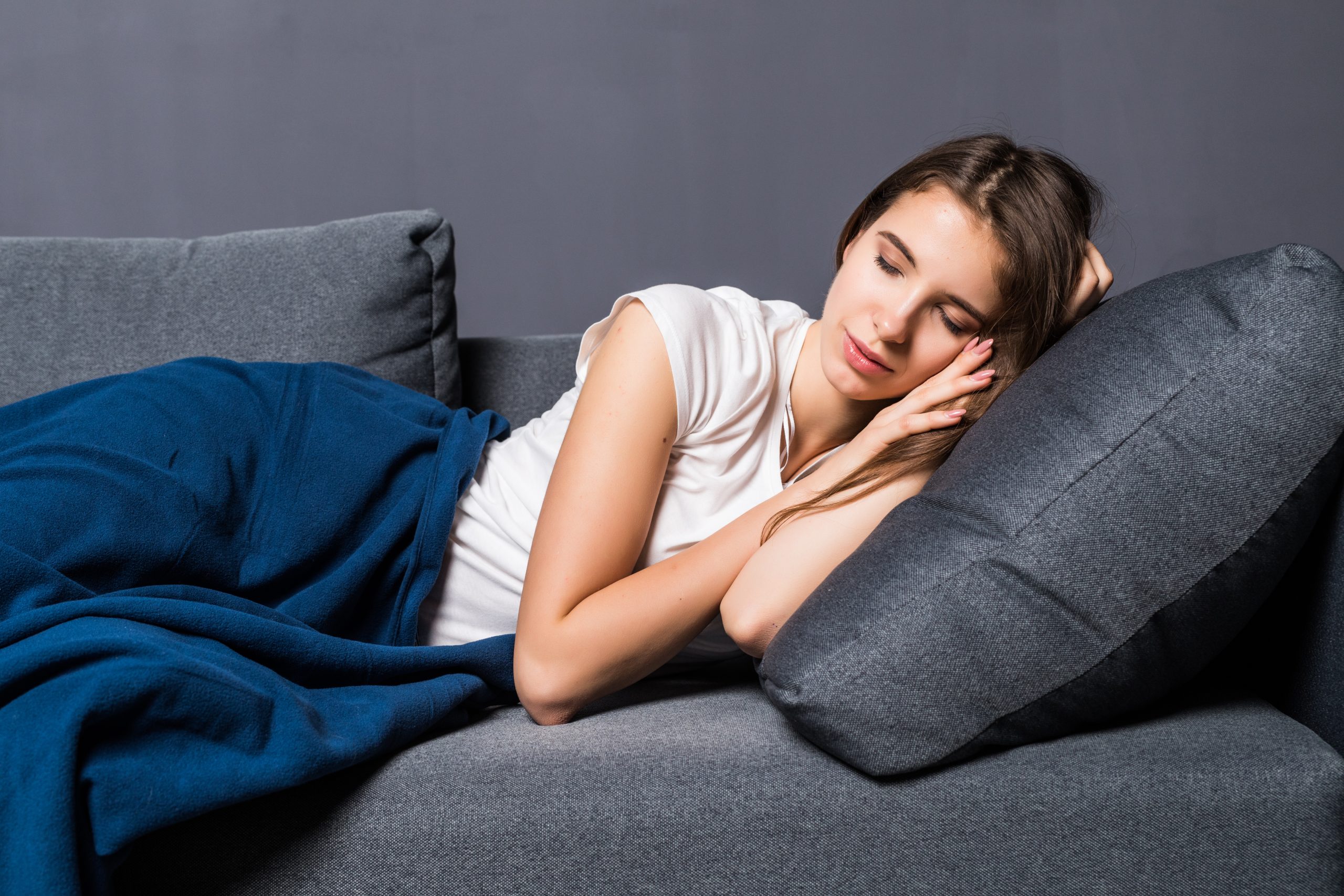 young girl sleeping sofa covered with blue blanker on a gray background
